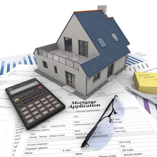 A house on top of a table with mortgage application form, calculator, blueprints, etc..